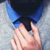Ein bärtiger Mann zieht unter dem V-Ausschnitt seines Pullovers die Krawatte zurecht