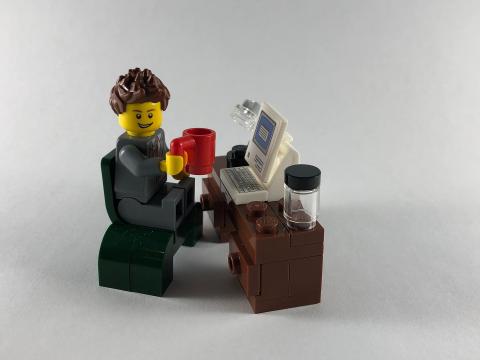 Spielzeug-Figur sitzt an einem Schreibtisch und trinkt Kaffee.